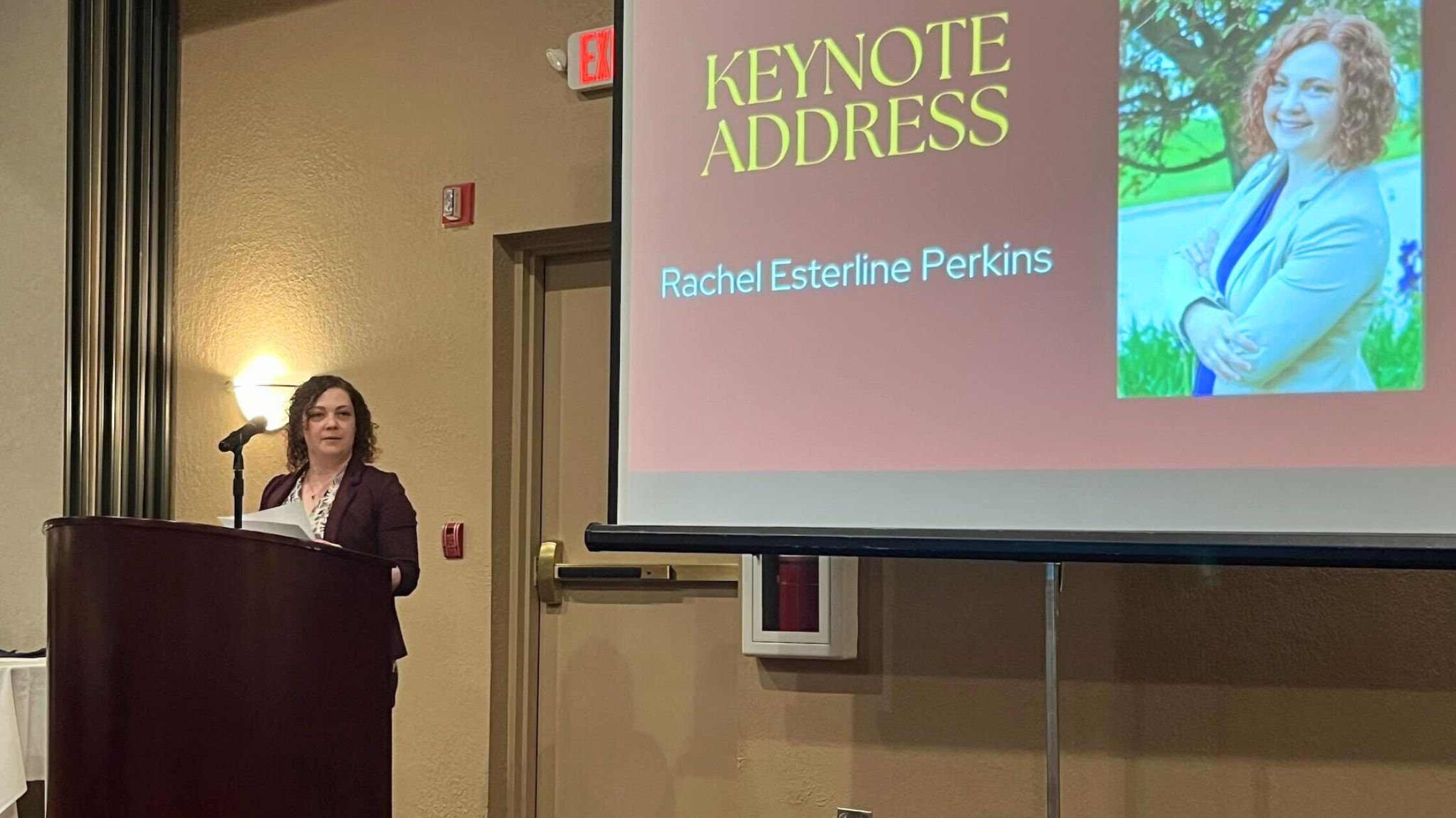 Rachel standing at a podium in front of a display that says "Keynote Address"